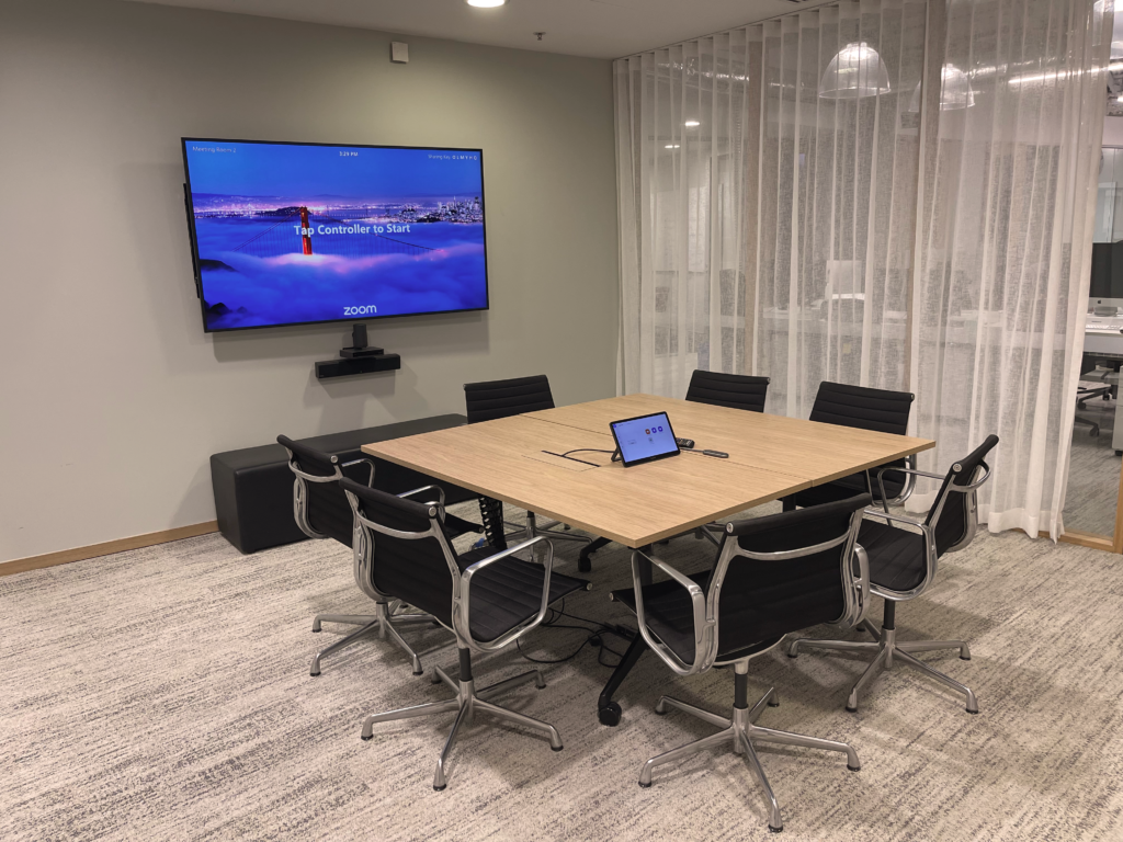 A meeting room with a blue TV screen and 7 chairs arranged around a table