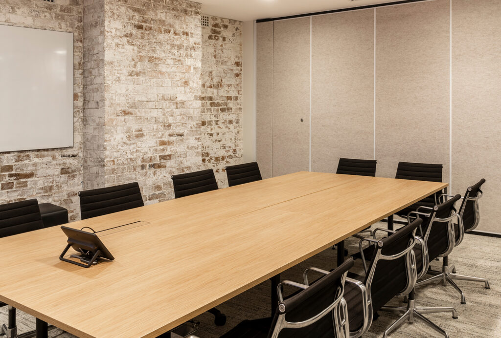 A meeting room with a big desk and 10 black chairs arranged around it